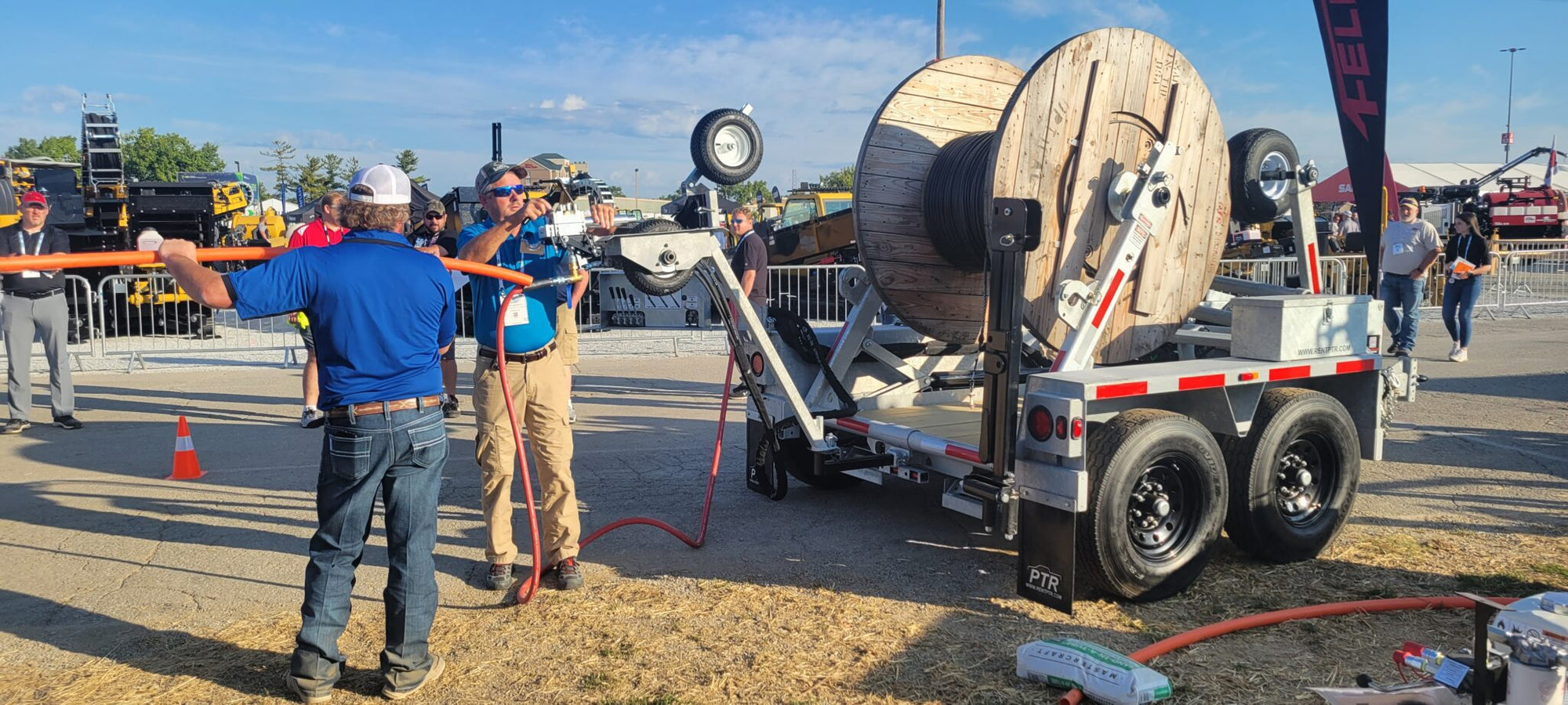 People working with a large spool of cable on a trailer at an outdoor event.